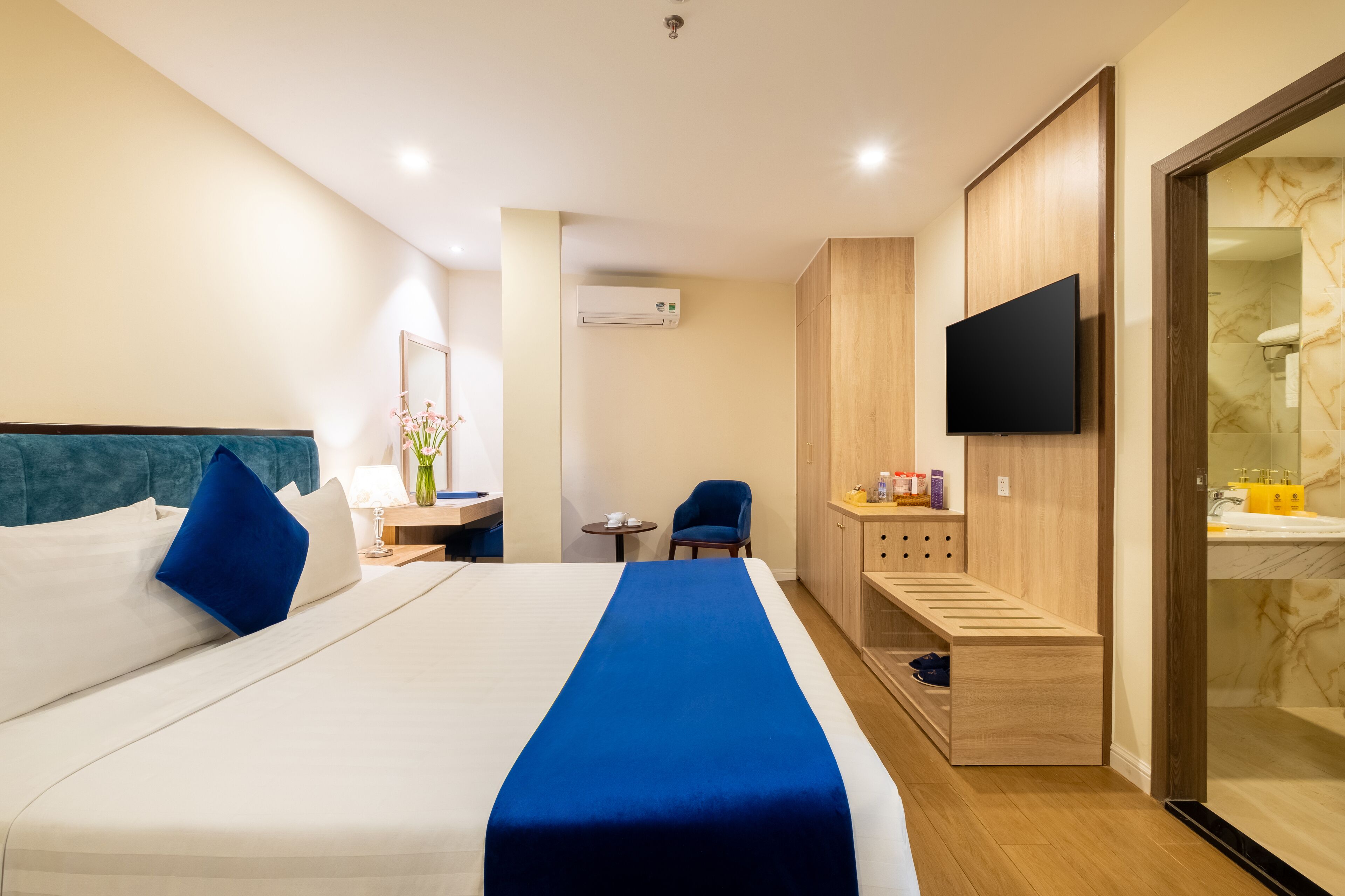 A hotel room with a bed, a desk, a chair, a TV, and a bathroom with a marble wall.