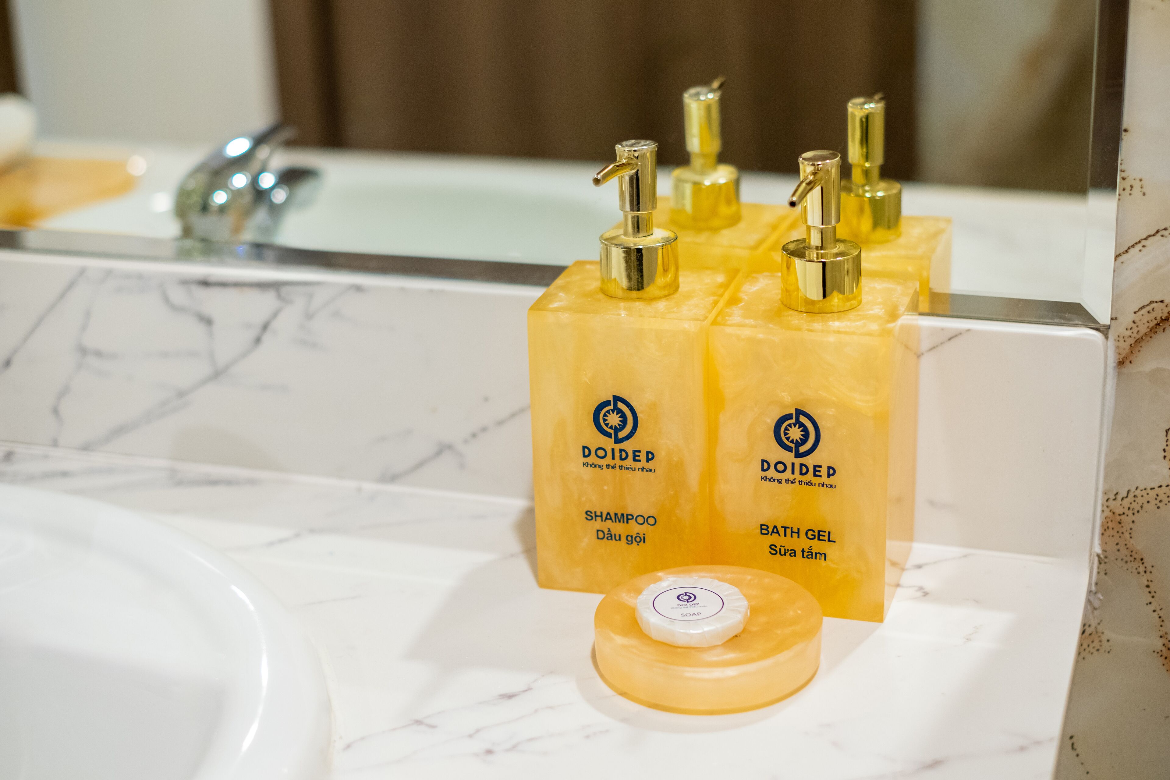 Un bagno con un lavandino in marmo e due flaconi gialli etichettati 'DOIDEP SHAMPOO' e 'DOIDEP BATH GEL' sul ripiano.