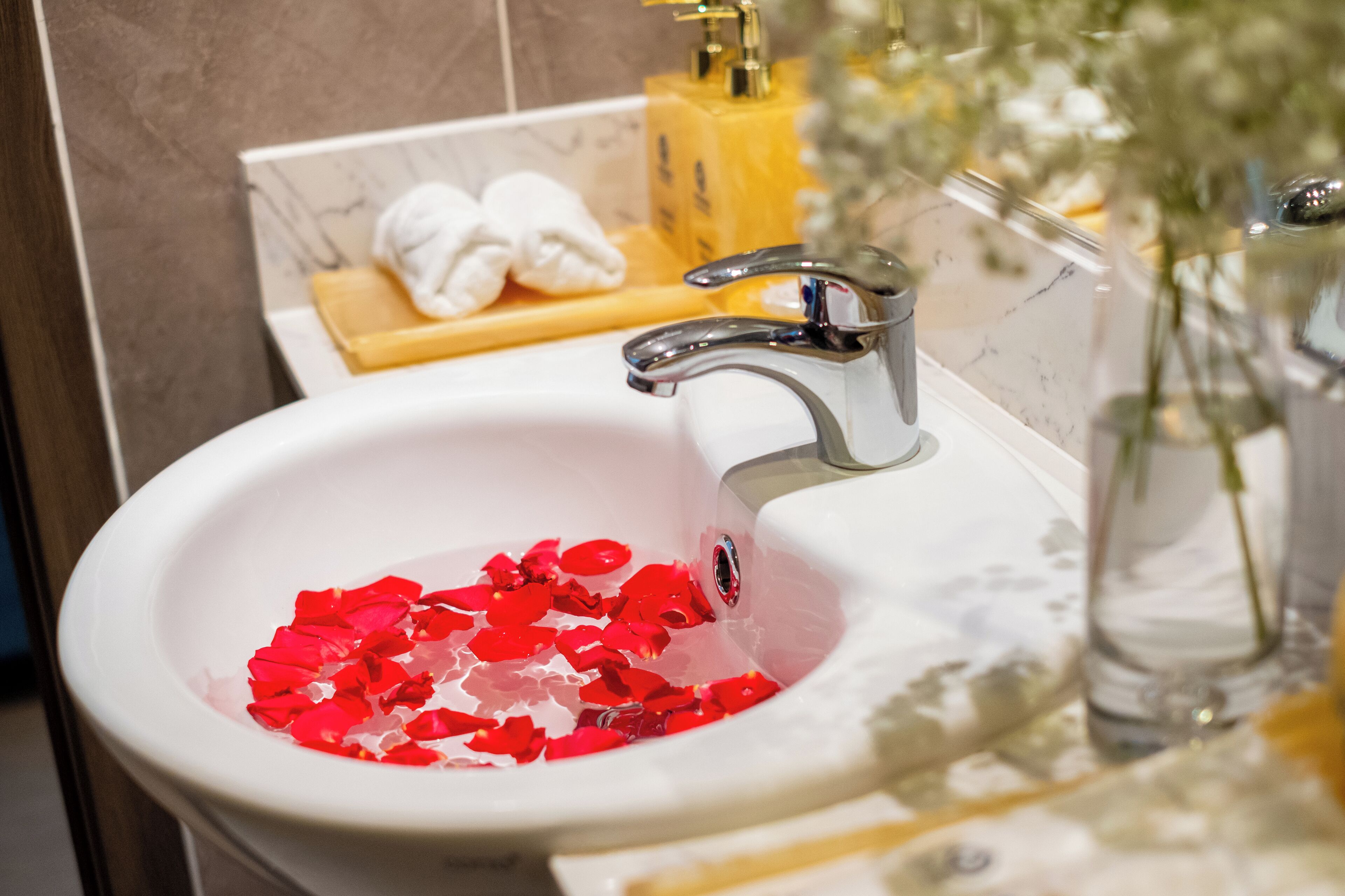 Un lavabo de salle de bain orné de pétales de roses rouges, une serviette blanche et un distributeur de savon jaune.