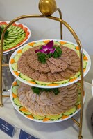 A multi-tiered platter with sliced meats and vegetables, displayed on a gold stand.