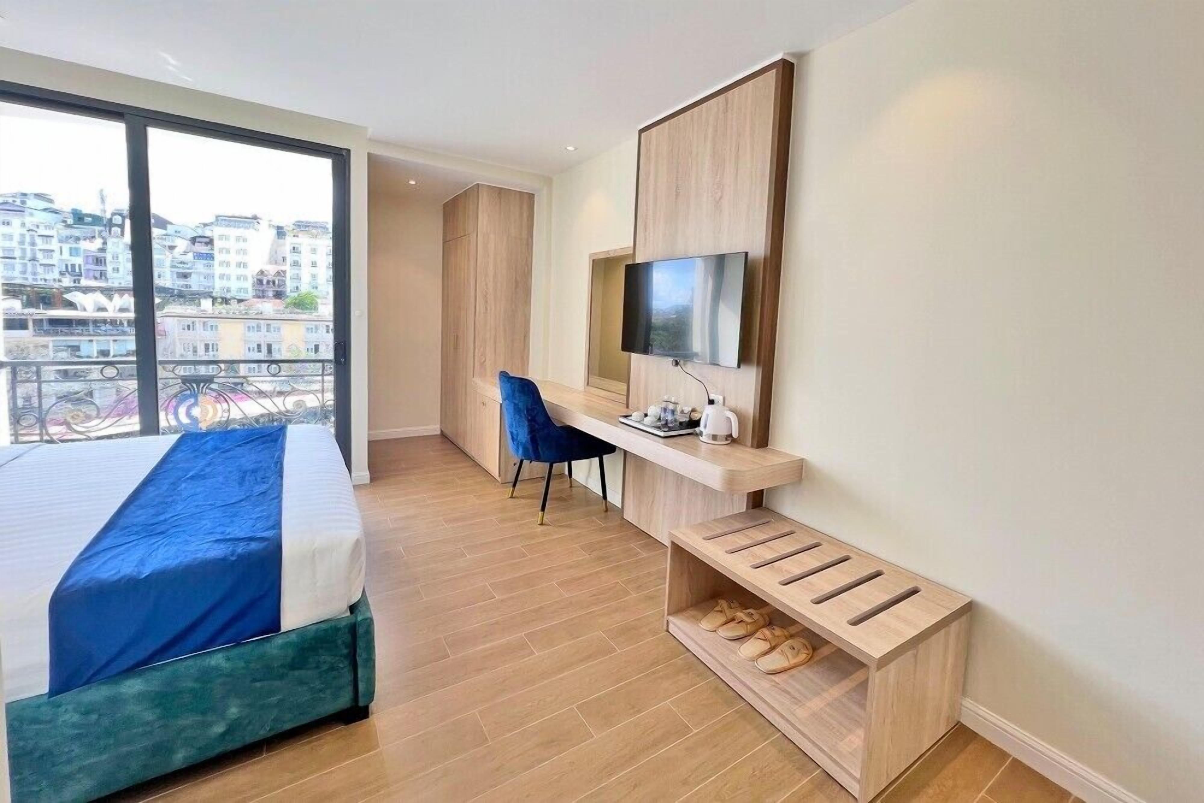 A modern hotel room with a bed, a desk, a chair, a TV, and a view of the city.