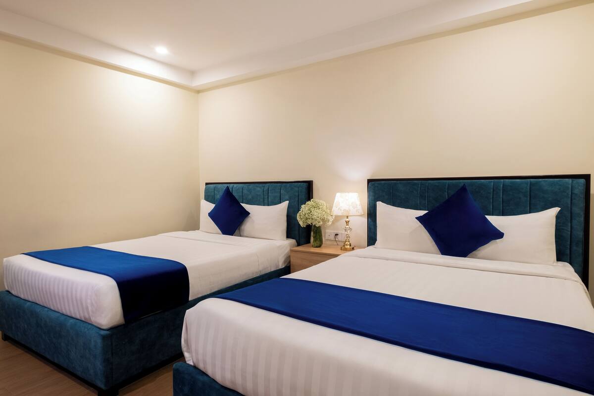 A hotel room with two beds, each with a blue headboard and white bedding.