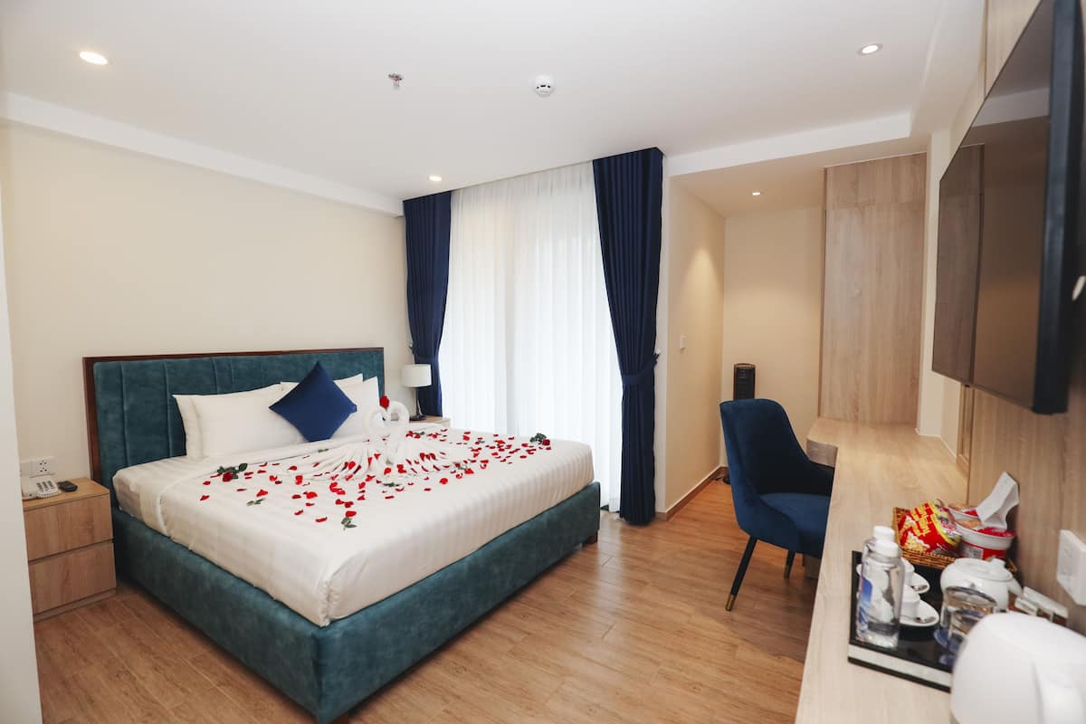 A hotel room with a large bed, a desk with a chair, a TV, and a minibar.