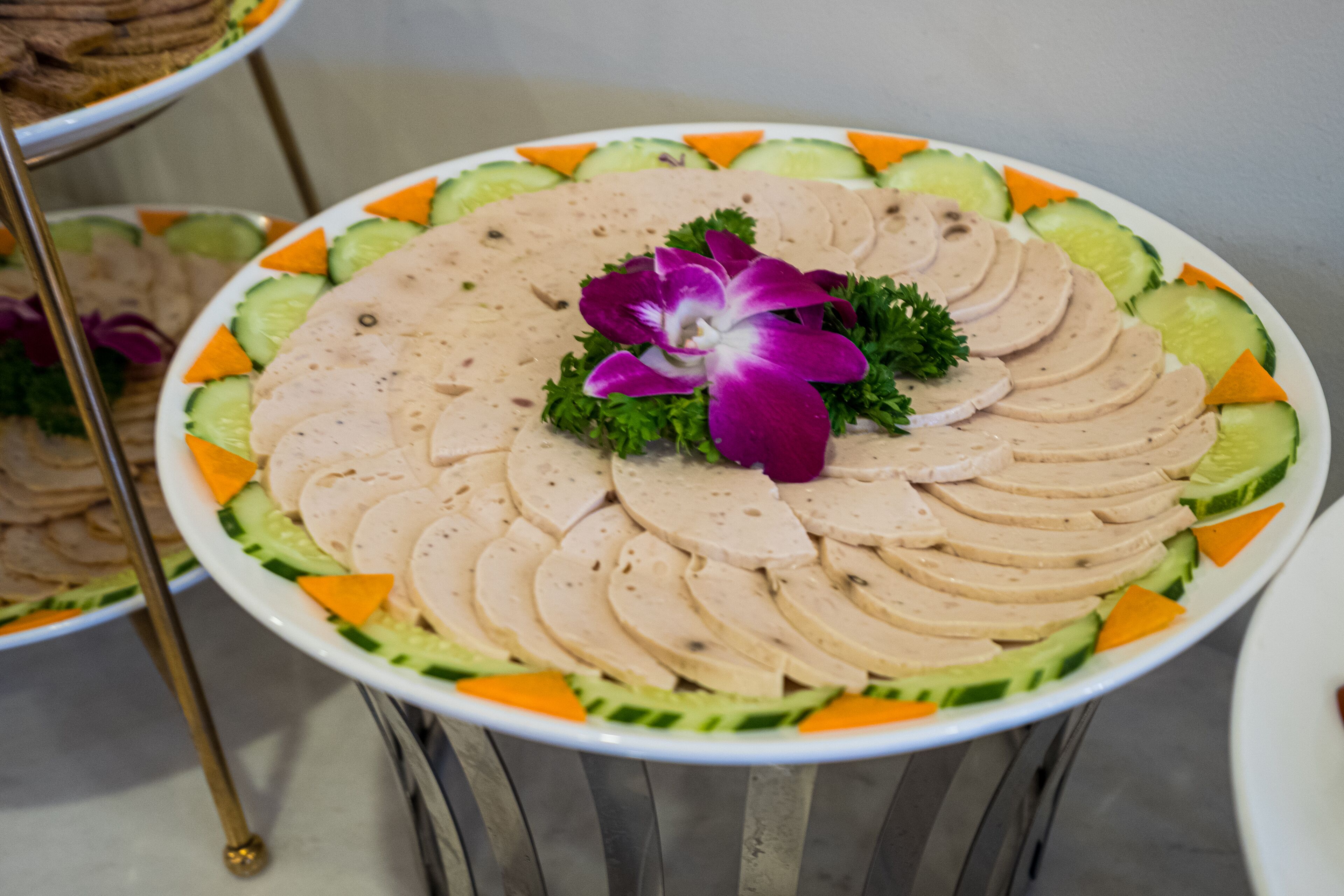 A round table with a plate of sliced meat and vegetables, garnished with a purple flower.