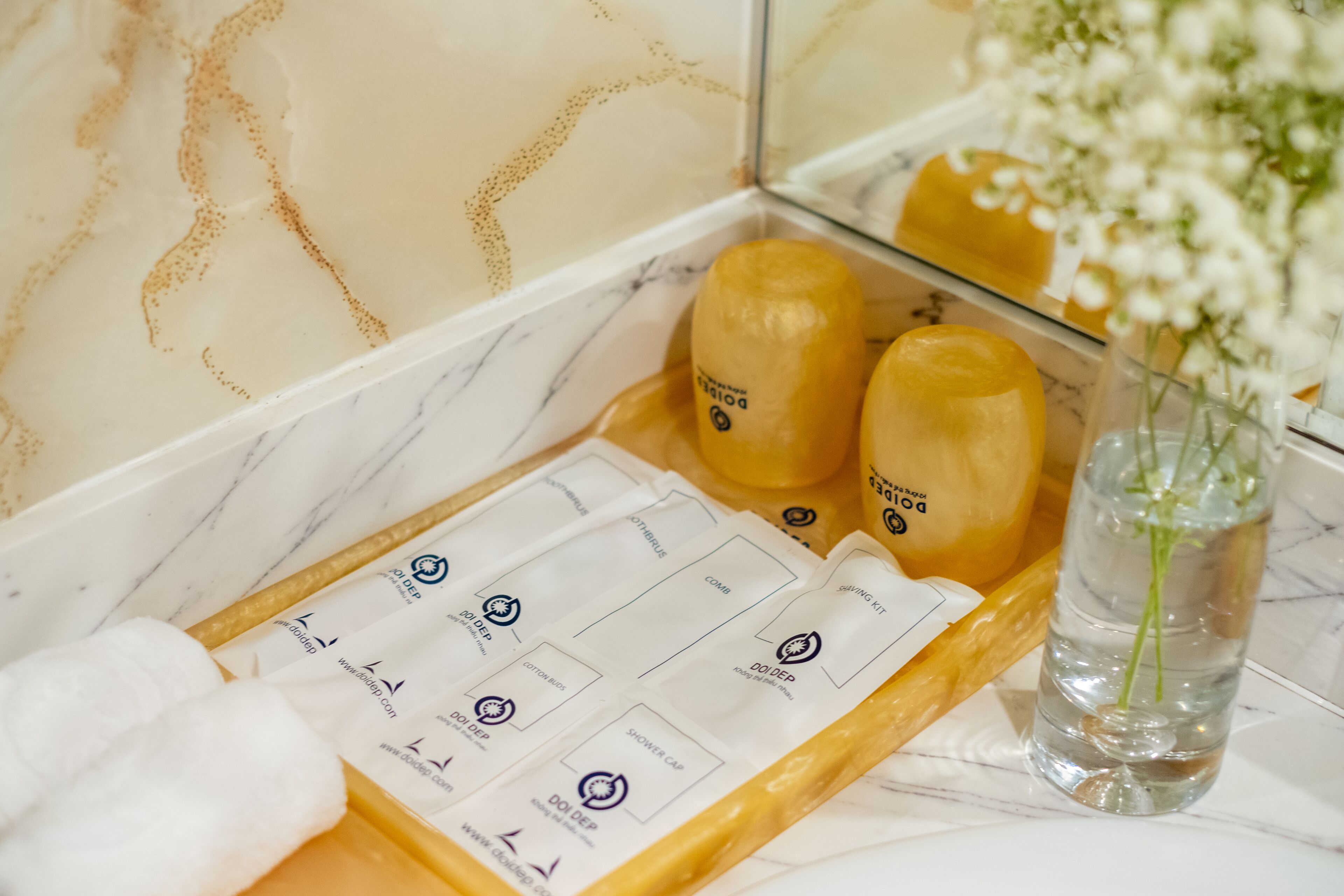 A bathroom vanity with toiletries, a towel, and a vase with flowers.
