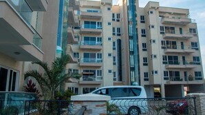 Un immeuble résidentiel à plusieurs étages doté de balcons, une voiture au premier plan et un ciel dégagé.