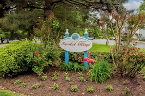 A sign for Sanibel Village surrounded by lush greenery and a pink flamingo statue.