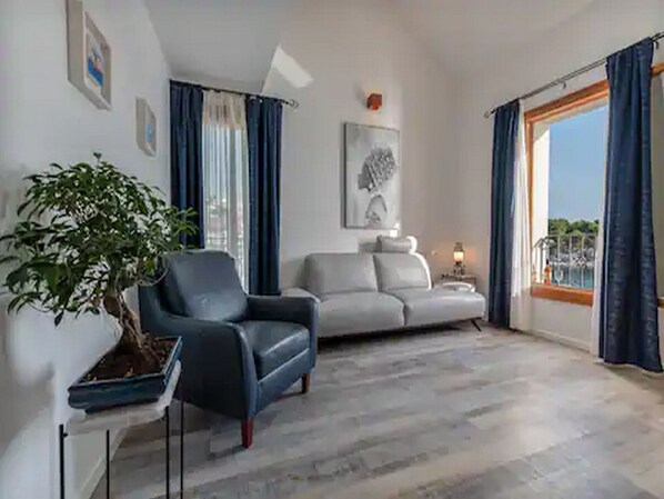Un salón con sofá, una silla, una planta y un cuadro en la pared.