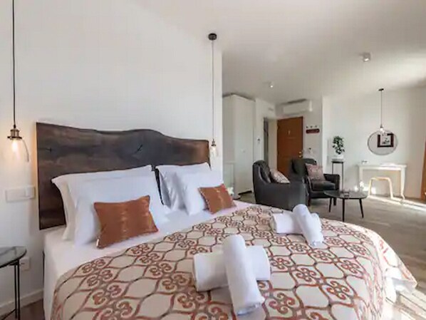 Una habitación de hotel con una cama grande, un cabecero de madera, una silla, una mesita y una chimenea.