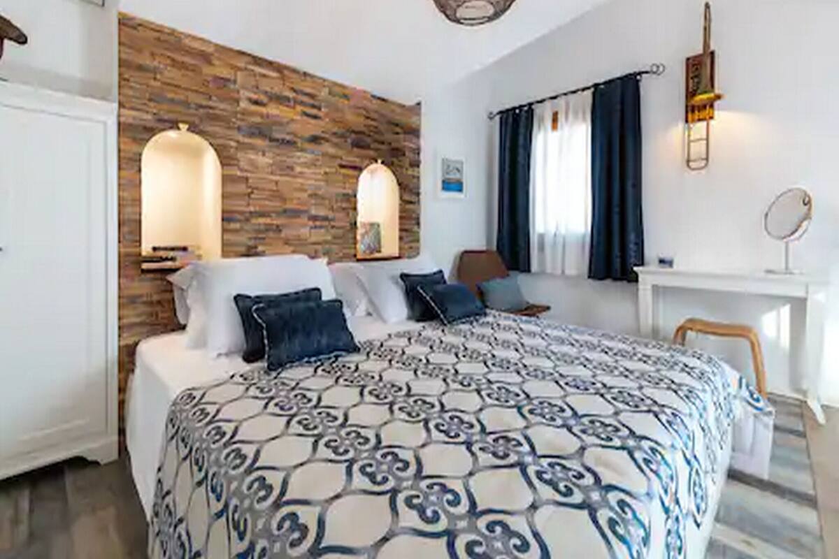 Un dormitorio con edredón estampado, pared de acento de madera, escritorio con espejo y ventana con cortinas.