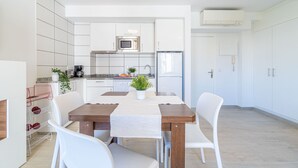 Une cuisine moderne avec des meubles blancs, un four à micro-ondes et un réfrigérateur. On y trouve une table à manger avec des chaises, et une plante en pot posée dessus.