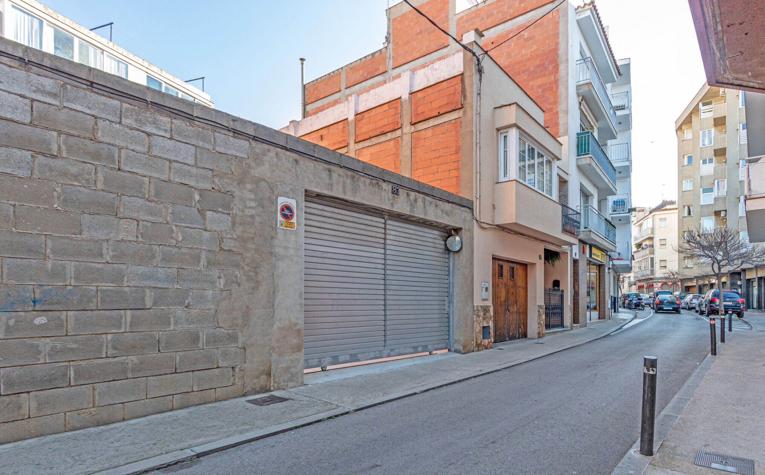 Straatbeeld met een gesloten metalen garage deur, een bakstenen muur en meerlaags gebouwen met balkons.