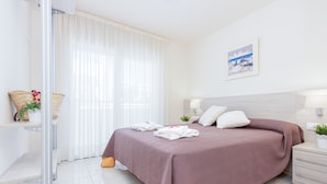 Une chambre à coucher moderne avec un grand lit, des tables de chevet, une fenêtre avec des rideaux légers et un tableau encadré au mur.