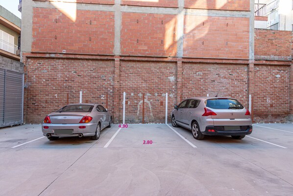 Zwei geparkte Autos auf einem Parkplatz, im Hintergrund eine Backsteinmauer.