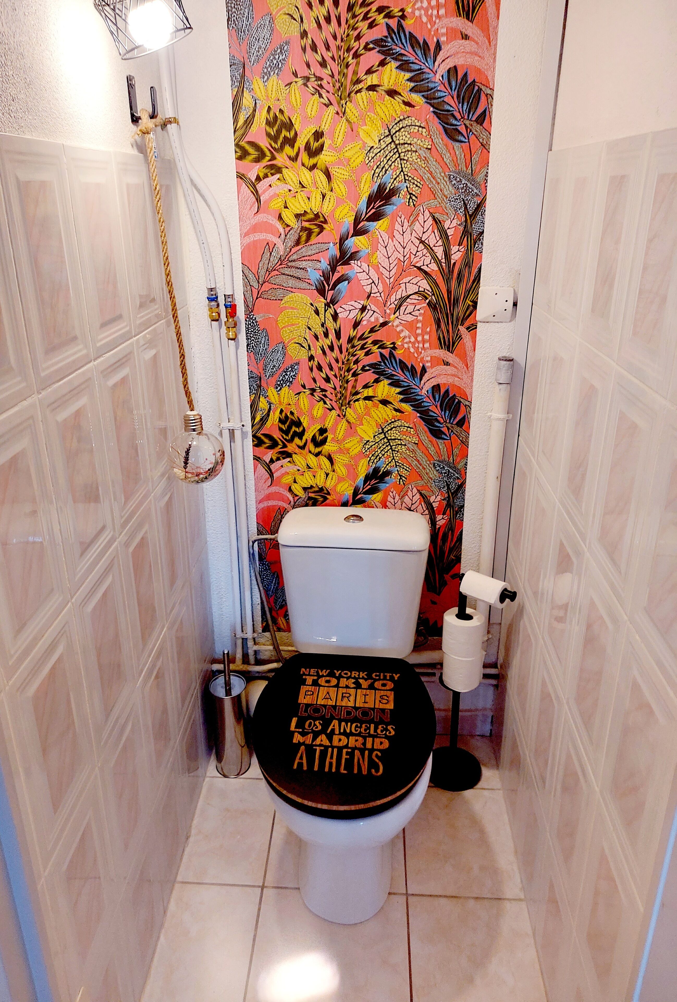 A bathroom with a toilet, a shower, and a wall with a floral pattern.