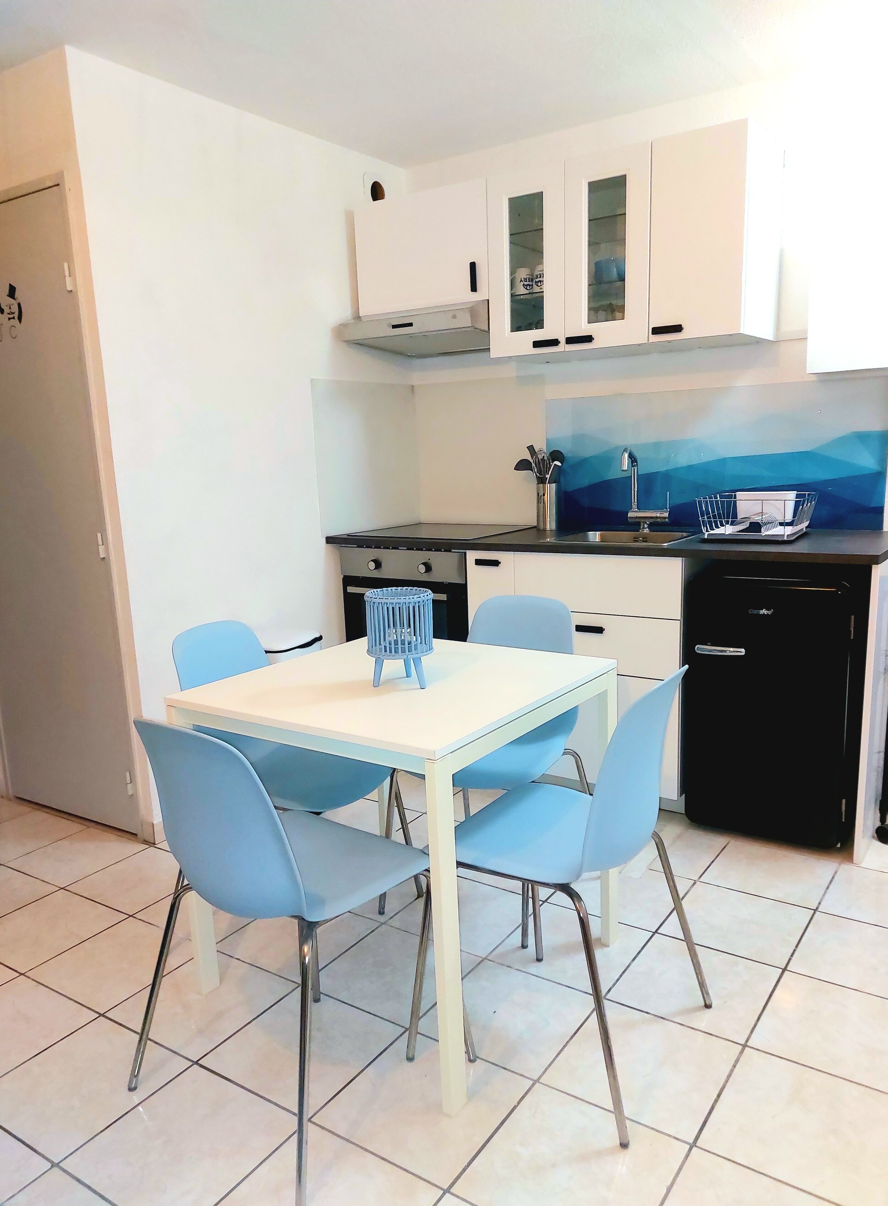 Una cocina compacta con armarios blancos, un refrigerador negro y una silla azul.