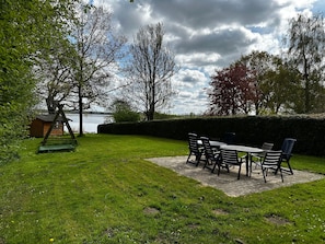 A patio with a table and chairs, a swing set, and a view of the water.