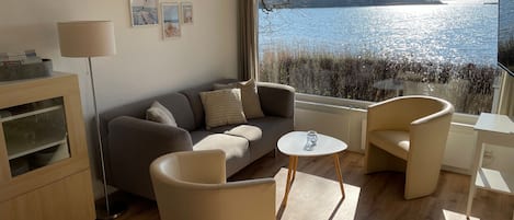 Een moderne woonkamer met een bank, fauteuils, een salontafel en uitzicht op een meer.