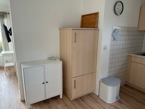 A compact kitchen with a wooden cabinet, a small trash bin, and a clock on the wall.