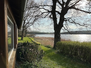 A view of a lake with a pathway leading to a grassy area, surrounded by trees and shrubs.