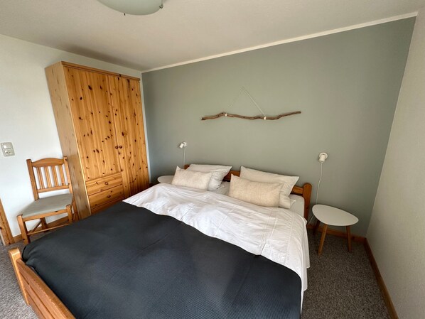 A bedroom with a bed, a wooden wardrobe, a chair, and a small bedside table.