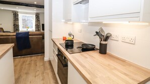 A modern kitchen with wooden countertops, a black induction cooktop, and a utensil holder. - Sparrow Cottage (Keswick)