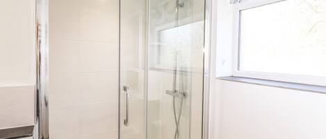A glass-enclosed shower with a handheld showerhead and a wall-mounted control panel.