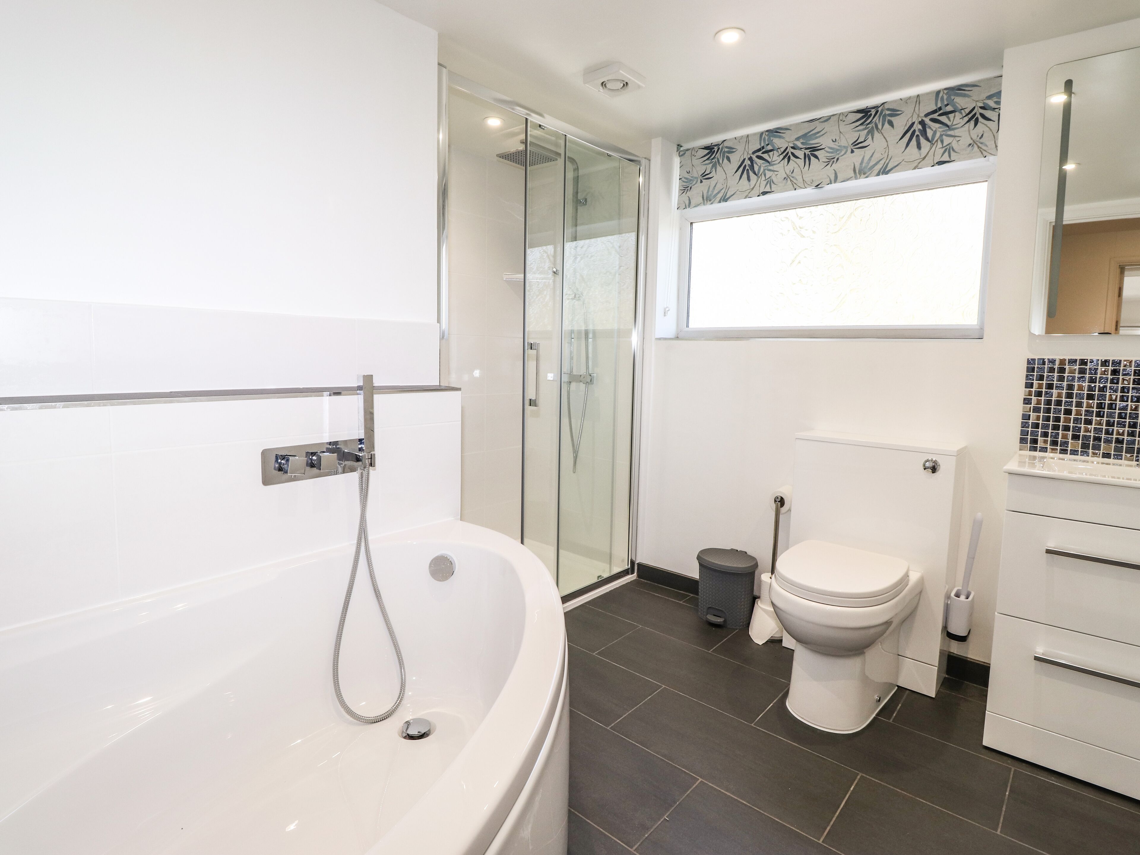 Un bagno moderno con doccia vetrata, una vasca freestanding, un water e un lavandino con pannello decorativo piastrellato.