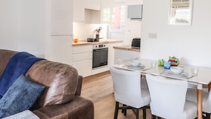 A modern kitchen with white cabinets, a dining table with chairs, and a brown leather sofa. - Sparrow Cottage (Keswick)
