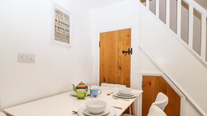 A dining area with a white table, chairs, and a wooden door. - Sparrow Cottage (Keswick)