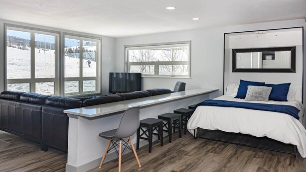 A modern hotel room with a large window, a sofa, a desk, and a bed. - Granby Ranch Lookout - 3bd/2ba Ski-in/out Luxury Slope-facing Mountainside Condo (Granby)