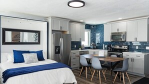 A modern bedroom with a bed, bedside table, and a large mirror. Adjacent to the bedroom is a compact kitchen with a refrigerator, microwave, stove, and a dining area with chairs. - Granby Ranch Lookout - 3bd/2ba Ski-in/out Luxury Slope-facing Mountainside Condo (Granby)