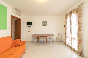Une pièce comprenant une table à manger, des chaises, un canapé, un téléviseur et une fenêtre avec des rideaux.
