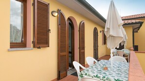 A yellow building with wooden shutters, a table with chairs, and a white umbrella. - Apartment "Bilocale Moraiolo" with Balcony, Shared Pool & Wi-Fi (Suvereto)
