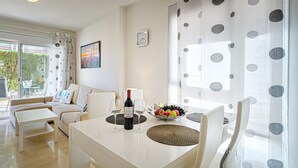 A modern living room with a dining table, white furniture, a clock on the wall, and a window with curtains. - Apartment 'Estrella 2 3 BH' close to the Beach with Shared Pool & Wi-Fi (l'Alfàs del Pi)