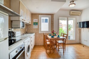 Une cuisine compacte équipée d’un four à micro-ondes, d’un grille-pain et d’un lave-linge. Une table à manger avec des chaises et un téléviseur fixé au mur.