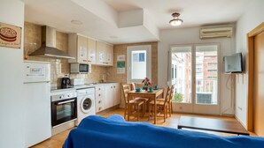 A compact kitchen with a microwave, stove, and washing machine, a dining area with a table and chairs, and a TV mounted on the wall. - Pet-Friendly Apartament Luisa close to the Beach with Balcony & Wi-Fi (Lloret de Mar)