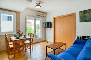 A living room with a blue sofa, wooden dining table, chairs, a TV, and a wooden wardrobe. - Pet-Friendly Apartament Luisa close to the Beach with Balcony & Wi-Fi (Lloret de Mar)