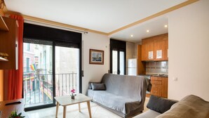 A living room with a sofa, a small table with a potted plant, a balcony with a railing, and a kitchen area with wooden cabinets. - Apartment Yaco 2 near the beach with sea views and Wi-Fi (Lloret de Mar)
