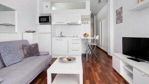 Un espacio habitable compacto con kitchenette, sofá, zona de comedor y televisor.