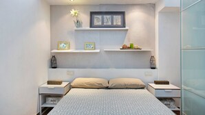Un dormitorio moderno con una cama grande, dos mesitas de noche, un estante en la pared con objetos decorativos e iluminación en el techo.