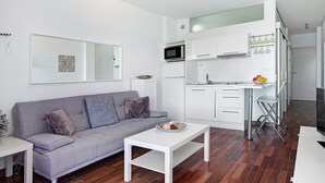 Un apartamento moderno con un sofá gris, una mesa de centro blanca y una cocina con armarios blancos y un microondas.