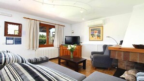 Ett vardagsrum med en soffa, fåtölj, soffbord, TV och öppen spis.