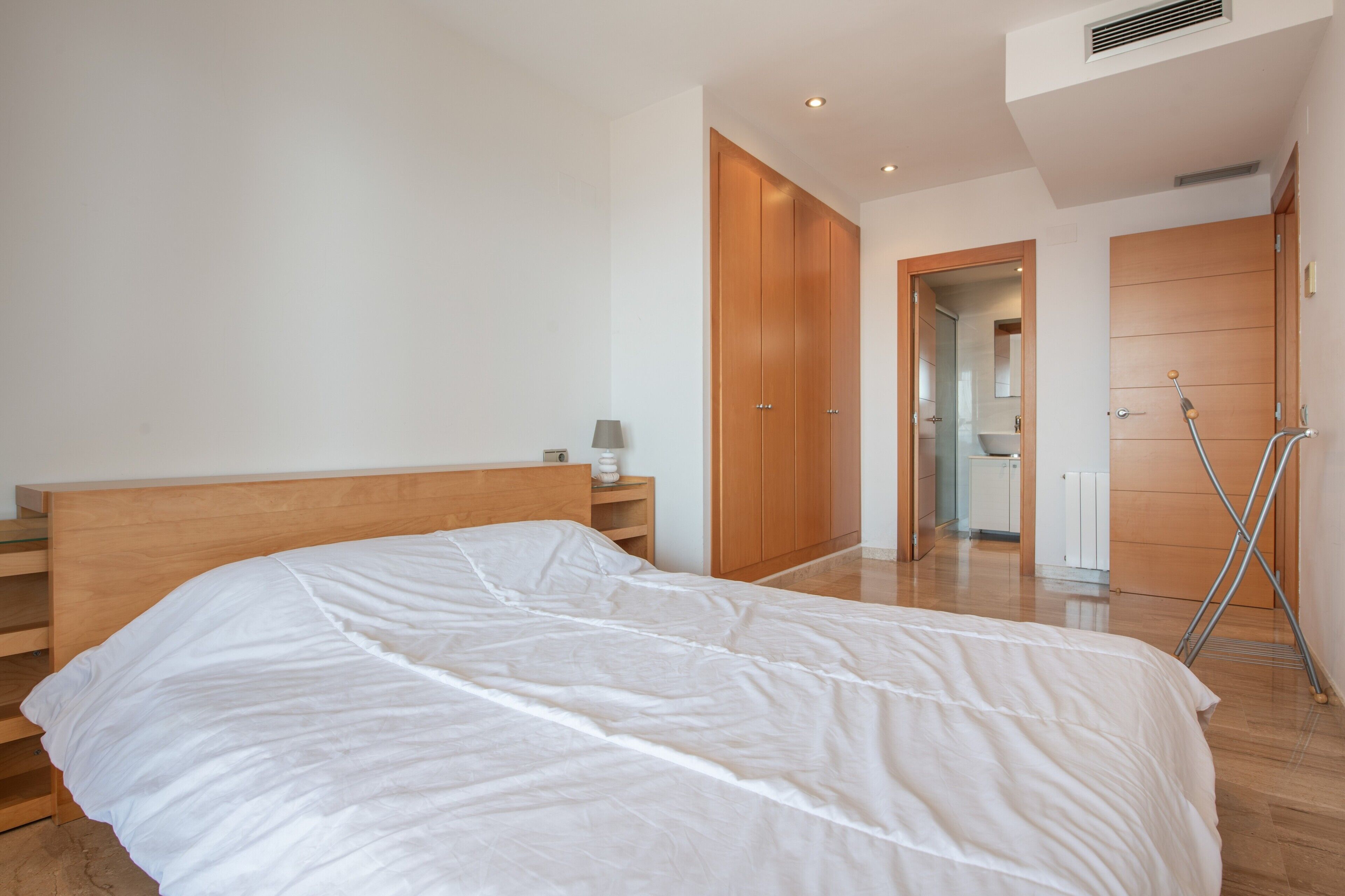 Een slaapkamer met een houten bed, nachtkastje, lamp en een kledingkast.