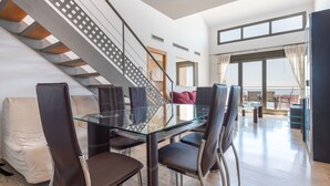 A modern living room with a glass dining table, leather chairs, a staircase, and a large window. - Apartment Sea and Pines with Sea View, Terrace, Shared Pools & Wi-Fi (Oropesa del Mar)
