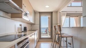 A modern kitchen with a built-in oven, microwave, and a coffee maker. There is a balcony with a view of the sea. - Apartment Sea and Pines with Sea View, Terrace, Shared Pools & Wi-Fi (Oropesa del Mar)