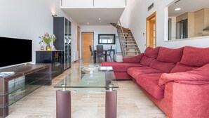 A modern living room with a glass coffee table, a red sofa, a flat-screen TV, and a staircase leading to an upper level. - Apartment Sea and Pines with Sea View, Terrace, Shared Pools & Wi-Fi (Oropesa del Mar)