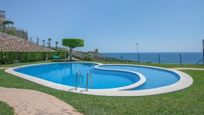 A swimming pool with a curved design, surrounded by a stone pathway and grass. - Apartment Sea and Pines with Sea View, Terrace, Shared Pools & Wi-Fi (Oropesa del Mar)