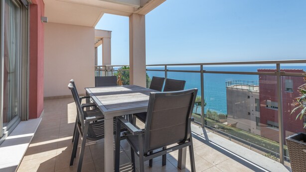 A balcony with a table and chairs, a view of the sea, and a building in the background. - Apartment Sea and Pines with Sea View, Terrace, Shared Pools & Wi-Fi (Oropesa del Mar)