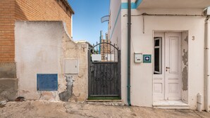 Une ruelle étroite, avec une entrée fermée par un portail, une porte blanche et une boîte aux lettres bleue.